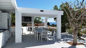 A modern outdoor kitchen with a dining area, a TV, and a view of the sea. - Modern luxury new build villa paradise, sea view, aircon, pool (Calpe)