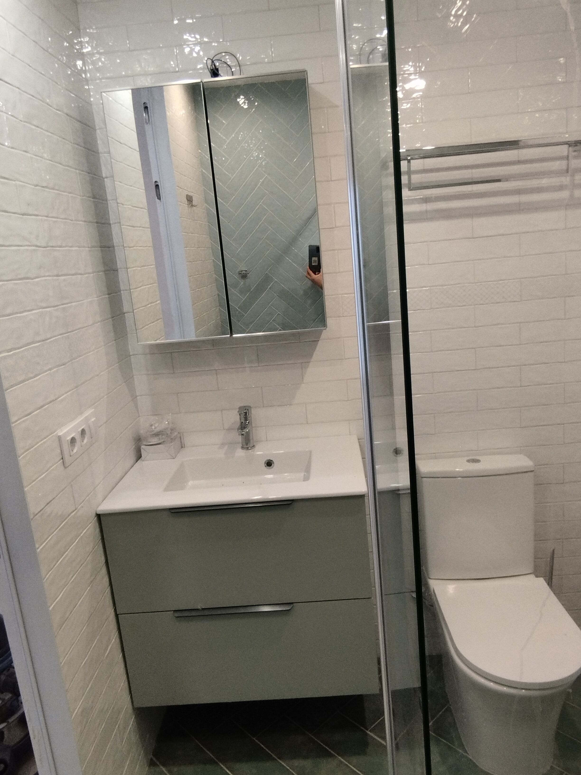 A bathroom with a glass shower enclosure, a white sink, a mirror, and a toilet.