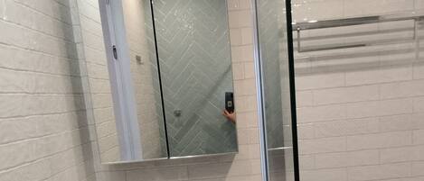 A bathroom with a glass shower enclosure, a white sink, a mirror, and a toilet.