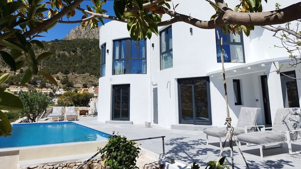 A modern white building with a pool, outdoor seating, and a mountainous backdrop. - Modern luxury new build villa paradise, sea view, aircon, pool (Calpe)