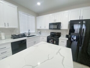 A modern kitchen with white cabinets, a black refrigerator, a microwave, and a stove.