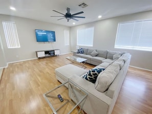 A modern living room with a grey sofa, a glass coffee table, and a ceiling fan.