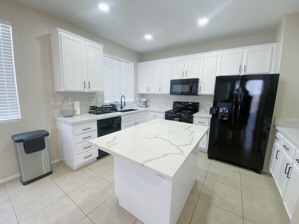 A modern kitchen with white cabinetry, a central island, a black refrigerator, and a microwave. - ☀Backyard Canal Access☀ Kayak + 5 Bedroom Home! (Moreno Valley)
