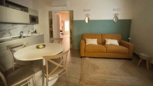 Un salon avec un canapé, une table à manger avec des chaises, un coin cuisine équipé d’un four à micro-ondes et un plafond avec des poutres apparentes.
