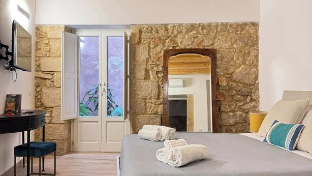 Une chambre à coucher avec un lit, un bureau, une chaise et un mur en pierre.