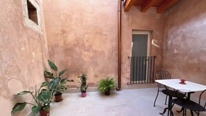 Une petite terrasse avec une table et des chaises, des plantes en pot et une porte.