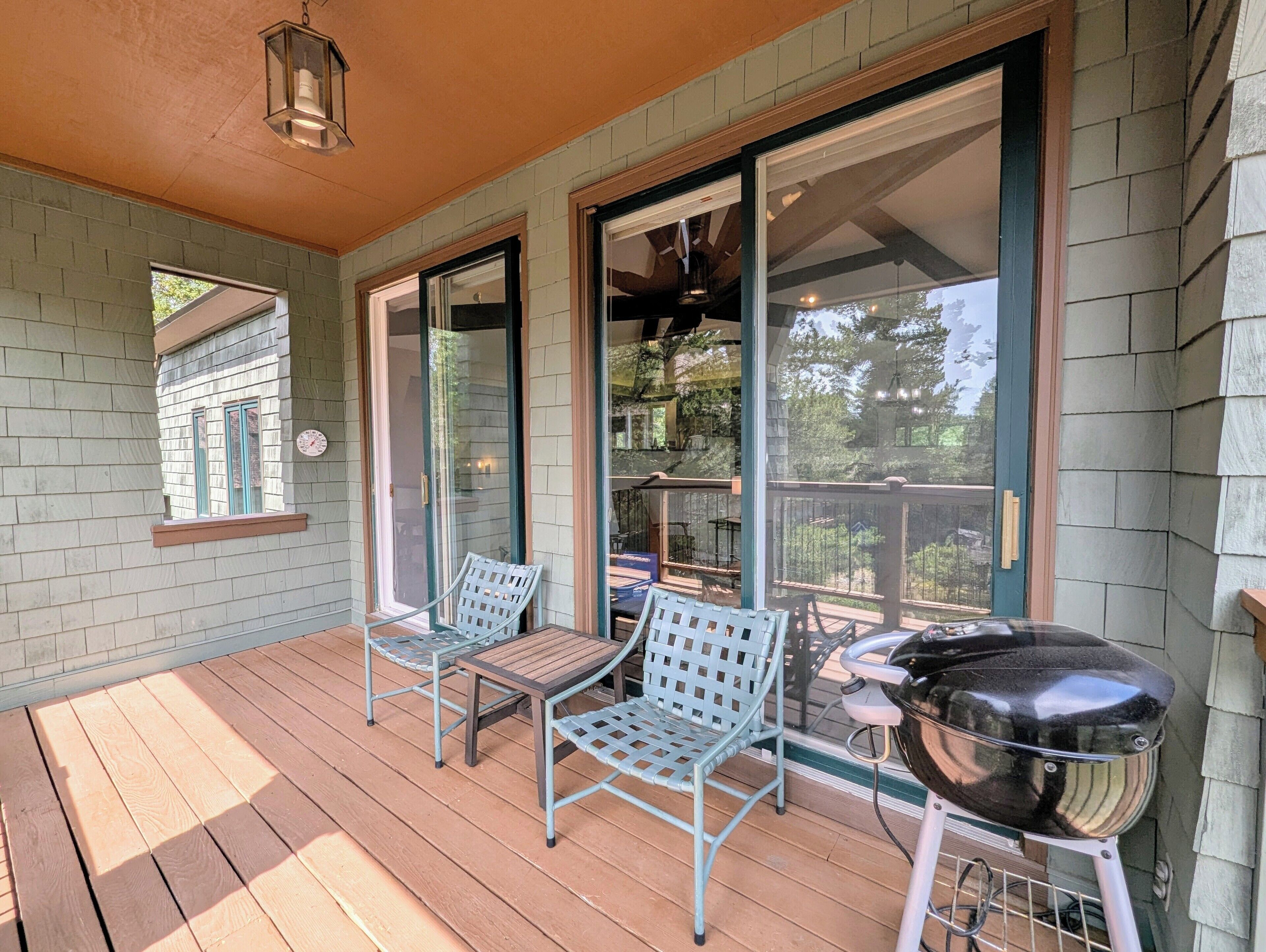 A covered porch with two chairs, a table, and a grill.