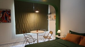Une pièce comprenant un lit, une table ronde avec des chaises, une lampe et un tableau accroché au mur.
