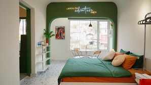 Une chambre avec un mur d’accent vert, un lit avec une literie orange, une fenêtre donnant sur un beau paysage, une petite table et une chaise.