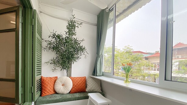 Une pièce avec un coin fenêtre, une plante en pot et une vue sur les bâtiments environnants.
