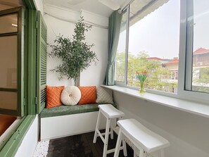 Une pièce avec un coin fenêtre, une plante en pot et une vue sur les bâtiments environnants.