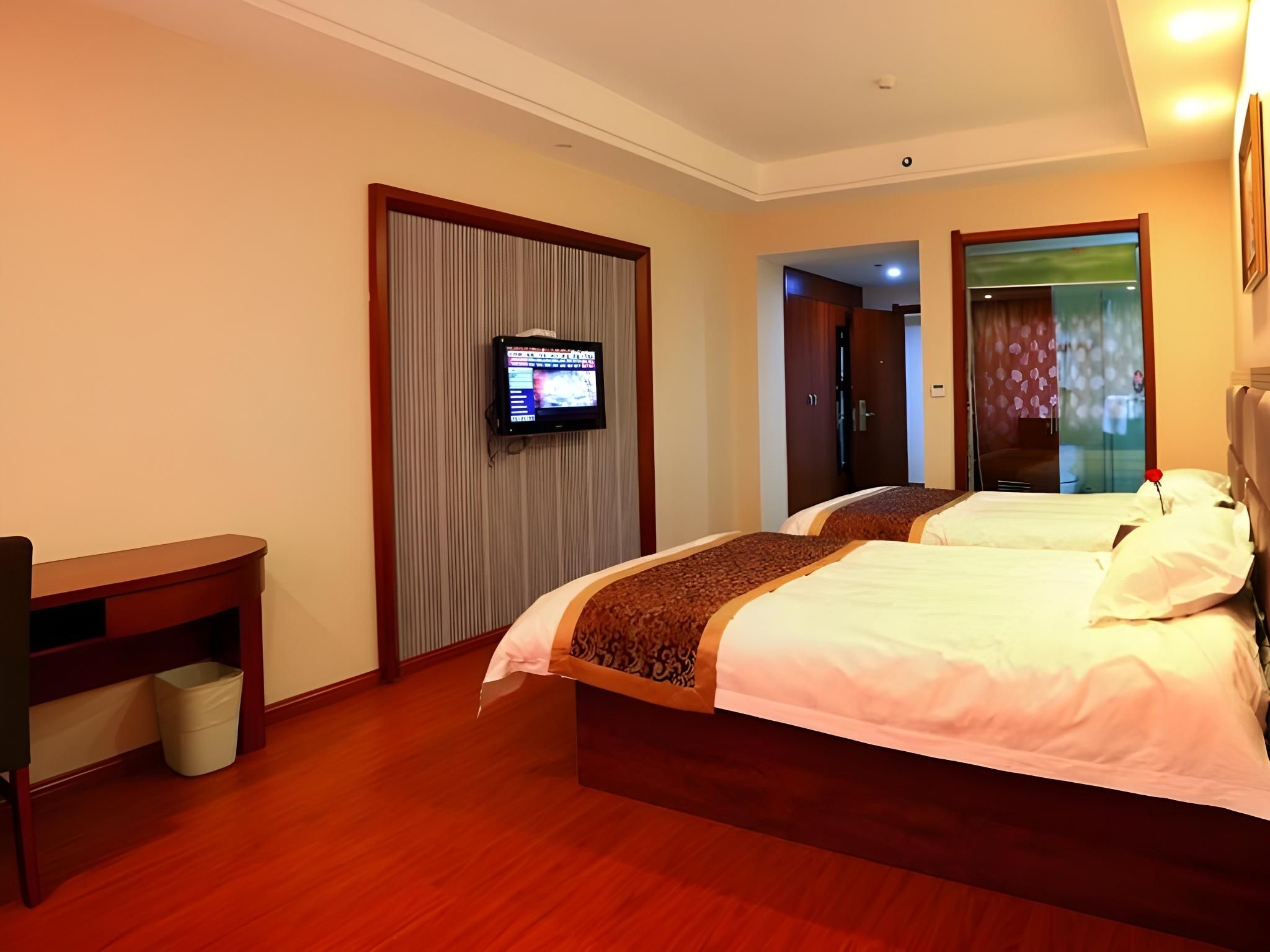 A hotel room with two beds, a television, a desk, and a trash bin.