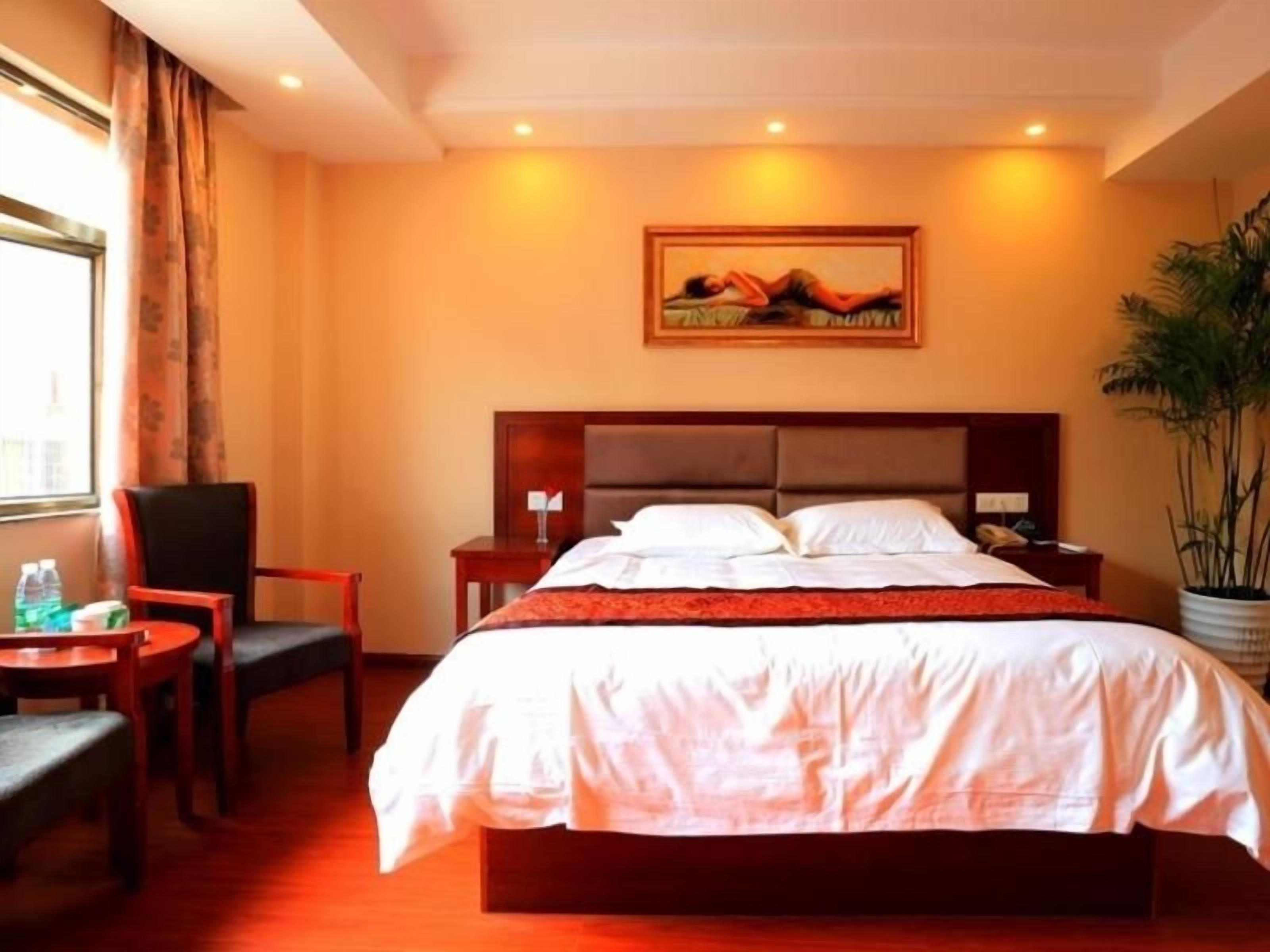 A hotel room with a large bed, a desk, a chair, a nightstand, and a window with curtains.