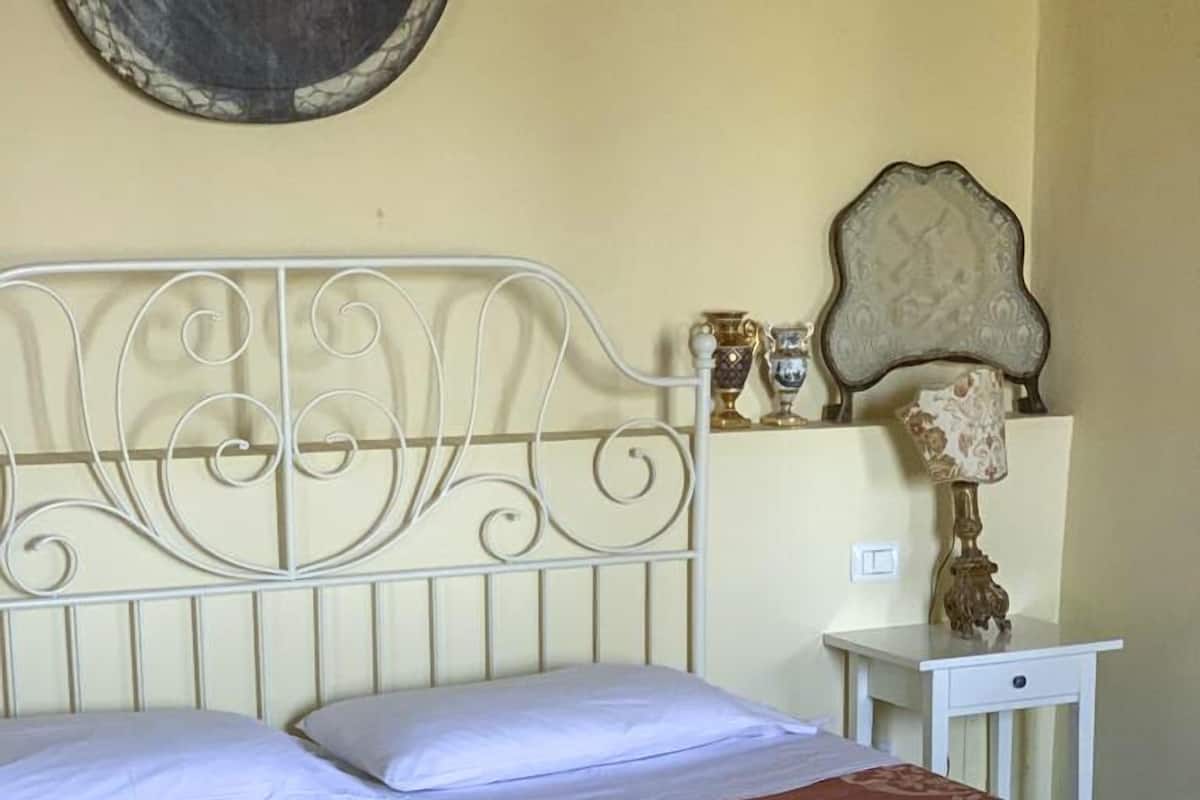 A bed with a metal headboard, a bedside table, and a mirror on the wall.