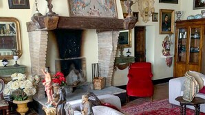 Un salón tradicional con chimenea, un sofá rojo y varios objetos decorativos, como estatuas y cuadros enmarcados.