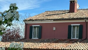 Una casa de dos plantas con tejado de tejas, contraventanas verdes y una pequeña chimenea.