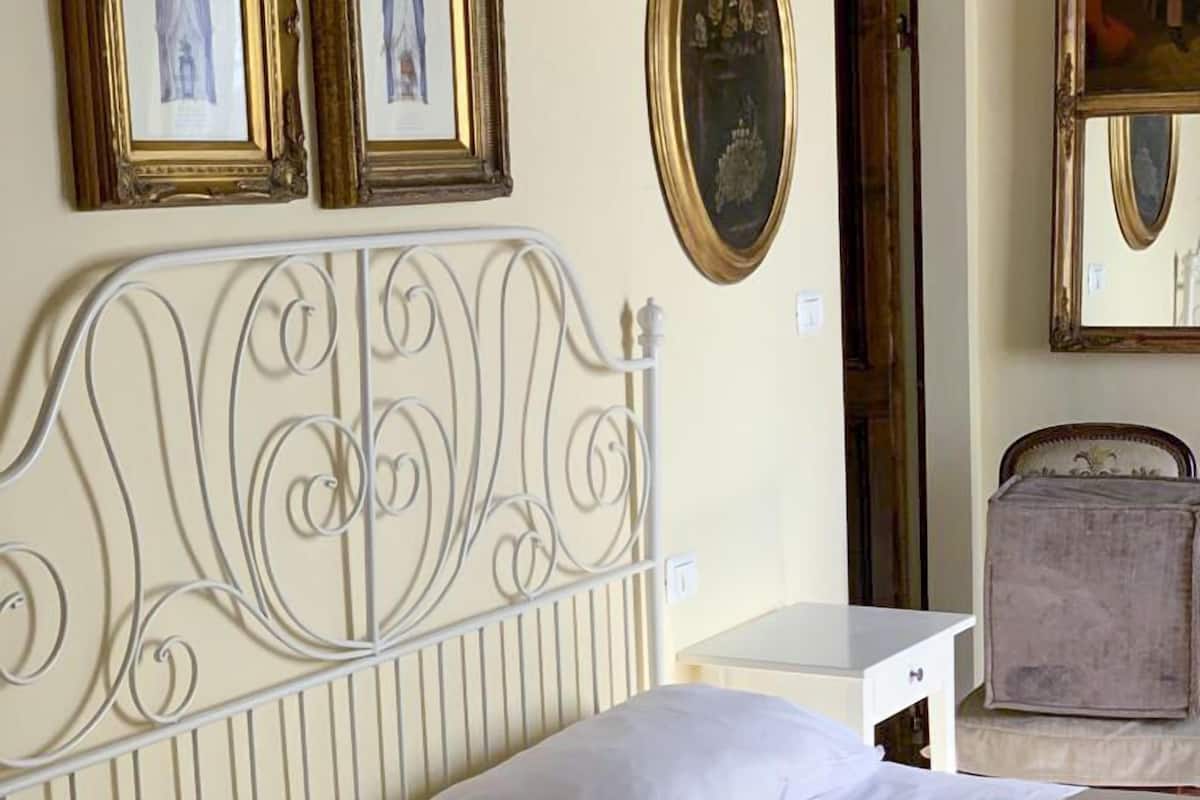 A bed with white linens, a metal headboard, and a bedside table with a drawer.