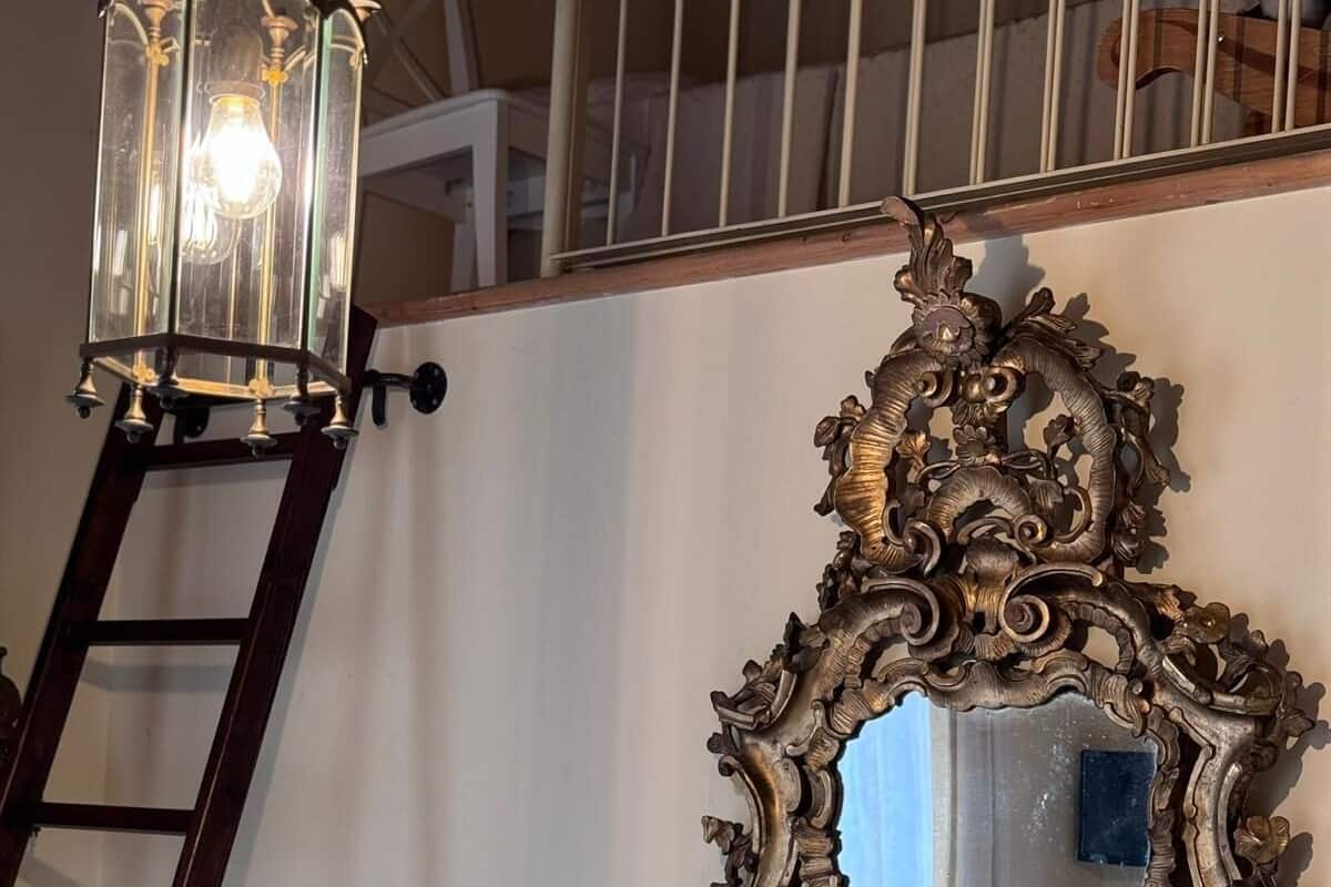 A bedroom with a white metal bed frame, a decorative mirror, a wooden ladder, and a wall-mounted light fixture.