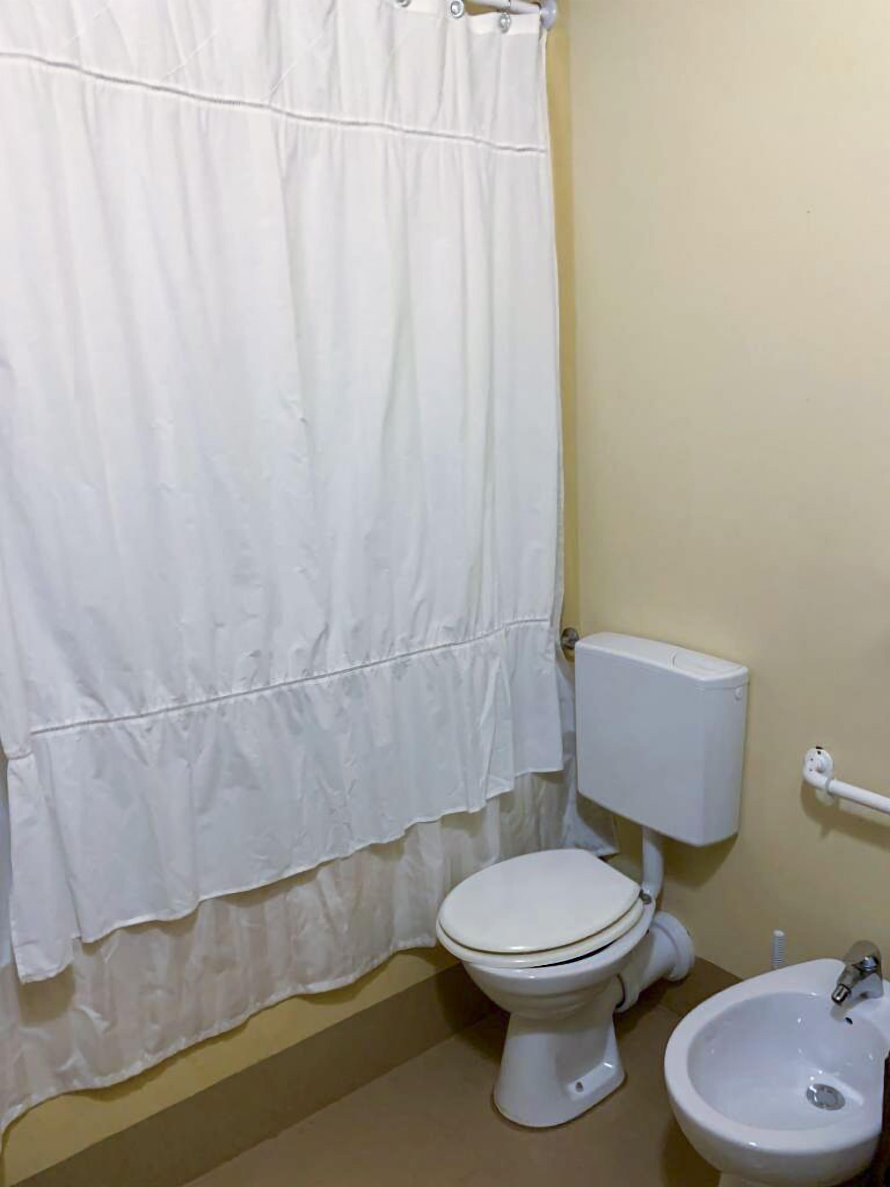 Un baño con inodoro, bidé y cortina de ducha blanca.