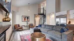 Una sala de estar moderna con un amplio sofá modular, una mesa de centro y una escalera que sube a un nivel superior.