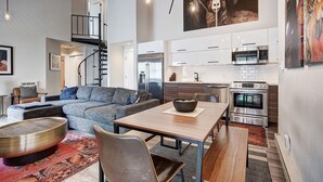 Un espacio habitable moderno con un sofá gris, una mesa de comedor de madera y una cocina con electrodomésticos de acero inoxidable.