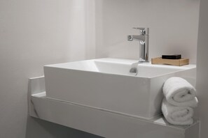 Ein modernes Badezimmer mit einem weißen Waschbecken, einem Chromarmaturen und einer Holzschatulle auf der Ablagefläche.