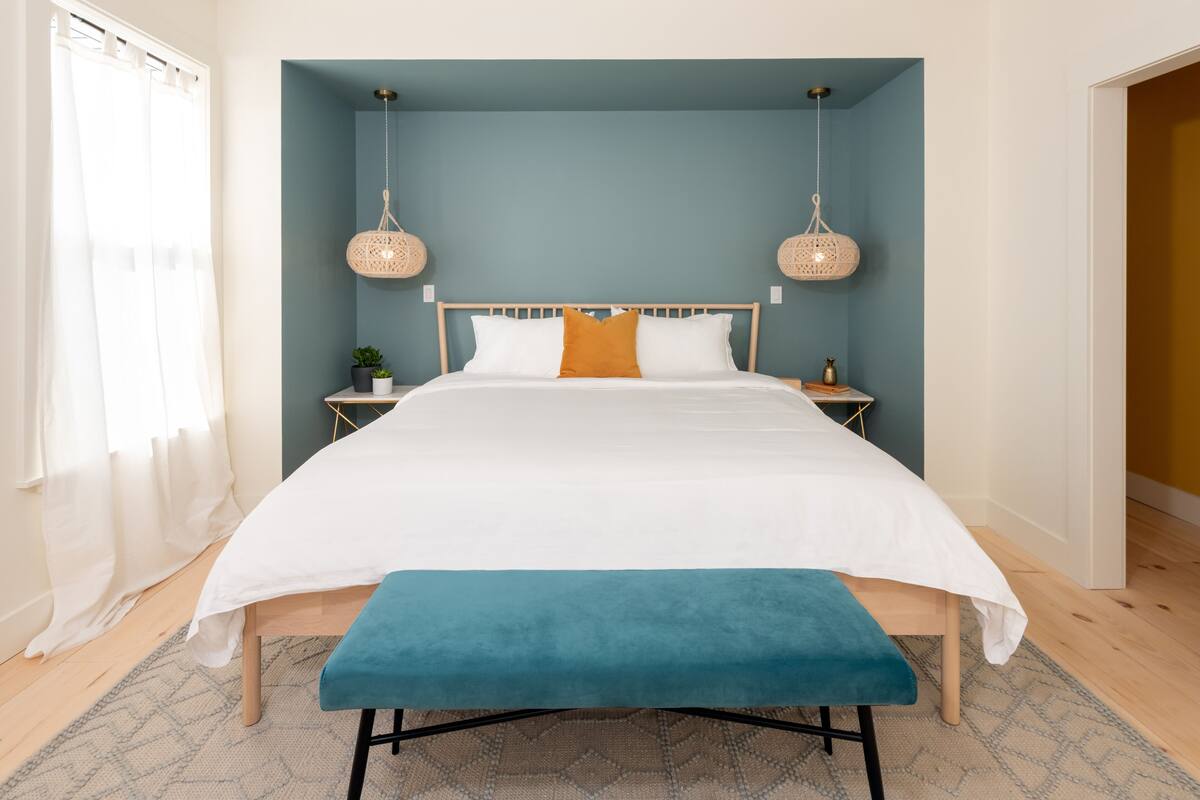A modern bedroom with a large bed, a bench, and two bedside tables with decorative lamps.