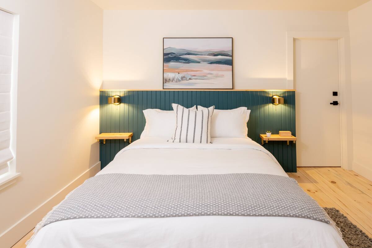 A neatly arranged bedroom with a large bed, two bedside tables, a wall-mounted lamp, and a framed picture above the bed.