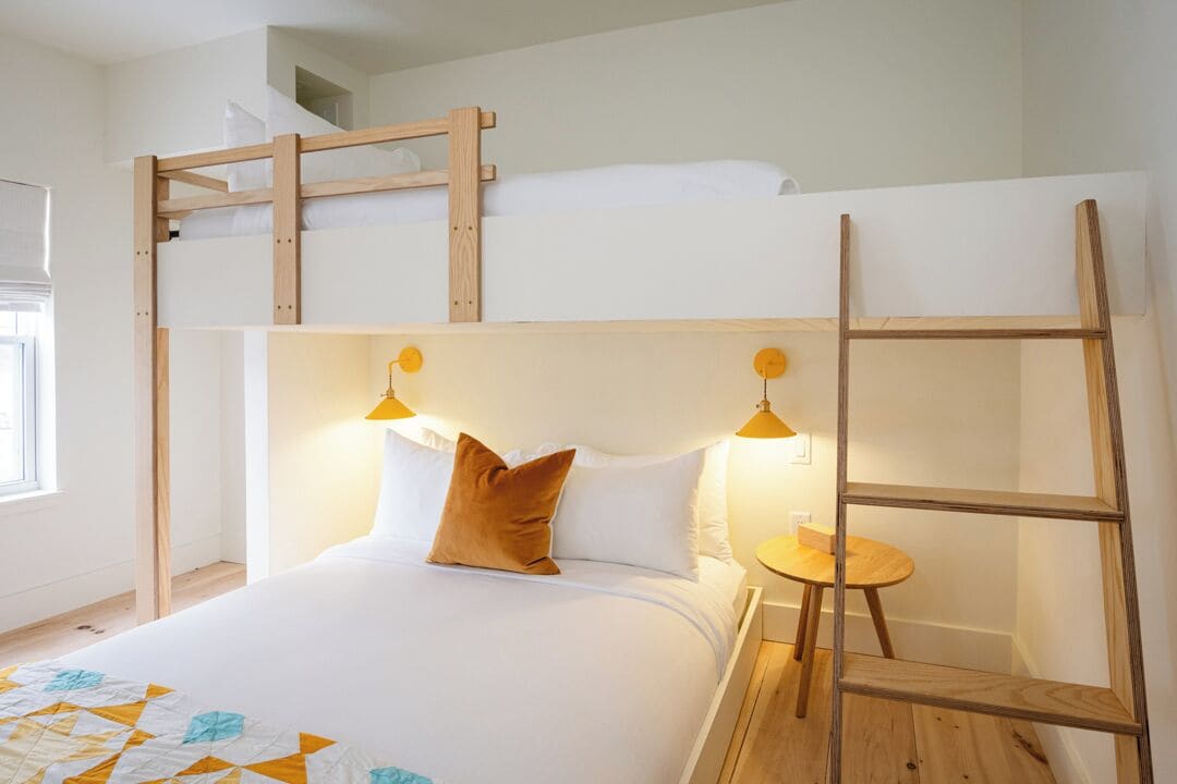 Una cama litera con escalera de madera, una mesita redonda y dos lámparas fijadas a la pared.