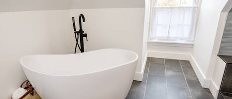 A modern bathroom with a freestanding bathtub, a window with a view, and dark tiled flooring.