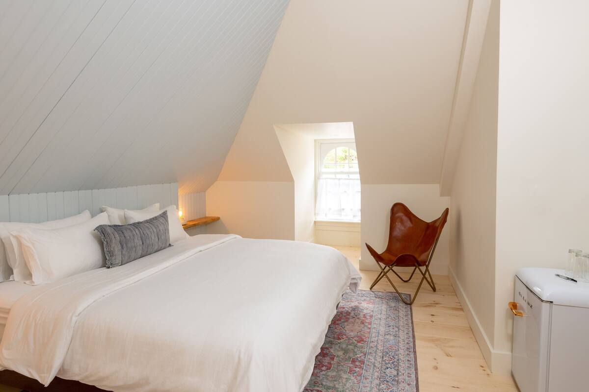 A bedroom with a bed, a chair, a small table, and a window.