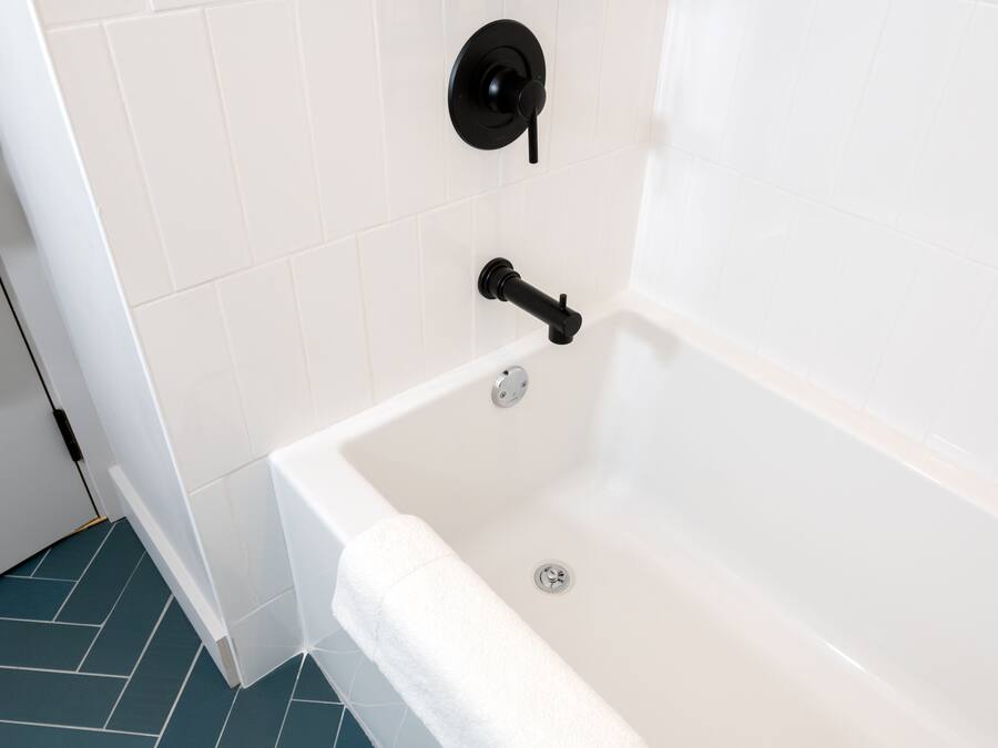Un baño moderno con una bañera blanca, un grifo negro y una toalla blanca en el borde.