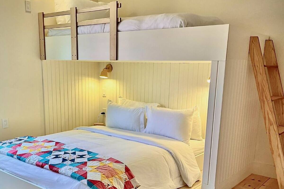 A bunk bed with a white headboard, a colorful quilt, and a bedside lamp.