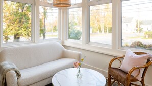 Ein Zimmer mit einem weißen Sofa, einem Korbstuhl, einem Marmortisch und einer Vase mit Blumen.