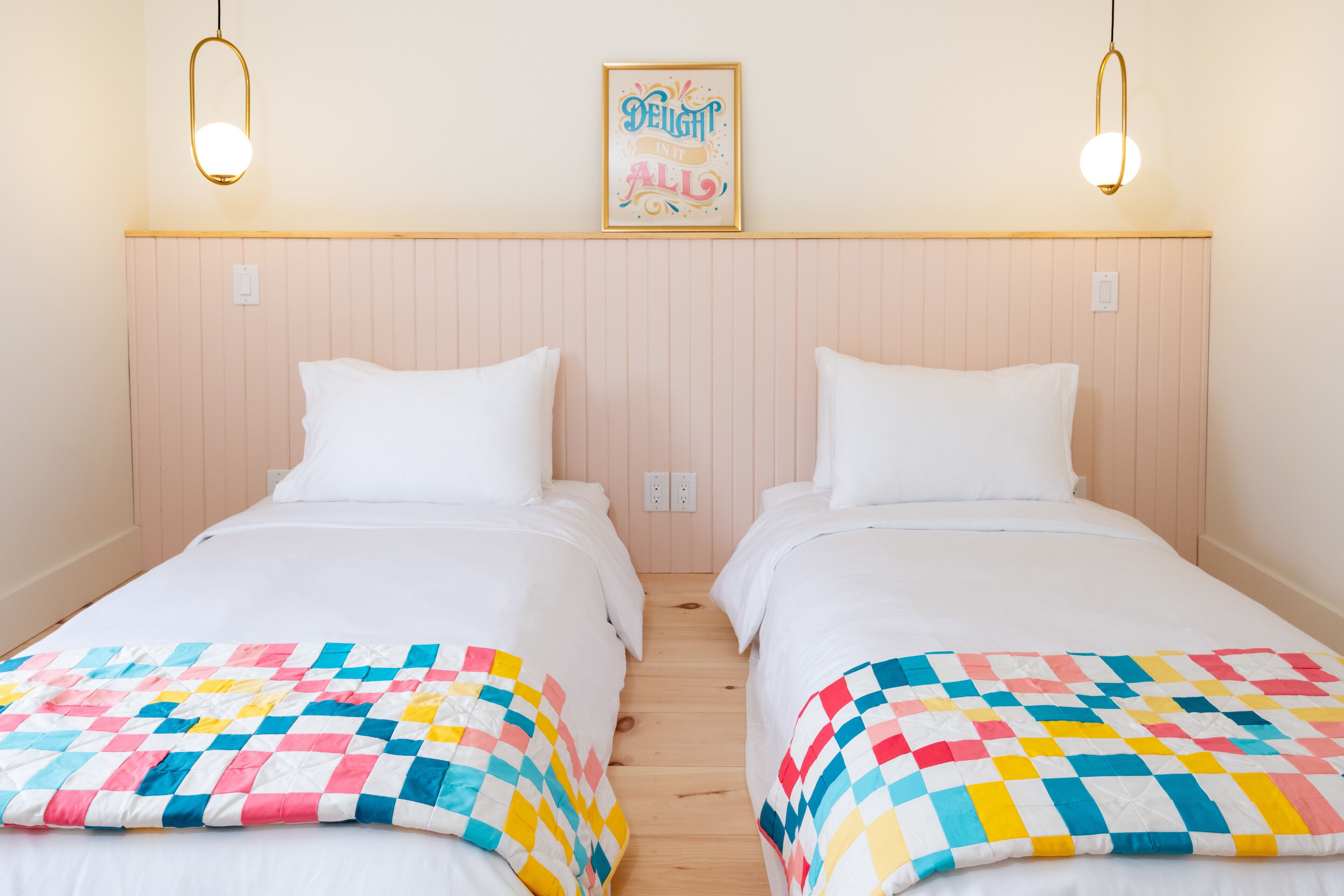 Habitación doble con dos camas, cada una con una colcha colorida, cabecero de madera y una lámpara de pared.