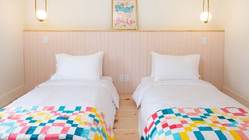 Habitación doble con dos camas, cada una con una colcha colorida, cabecero de madera y una lámpara de pared.