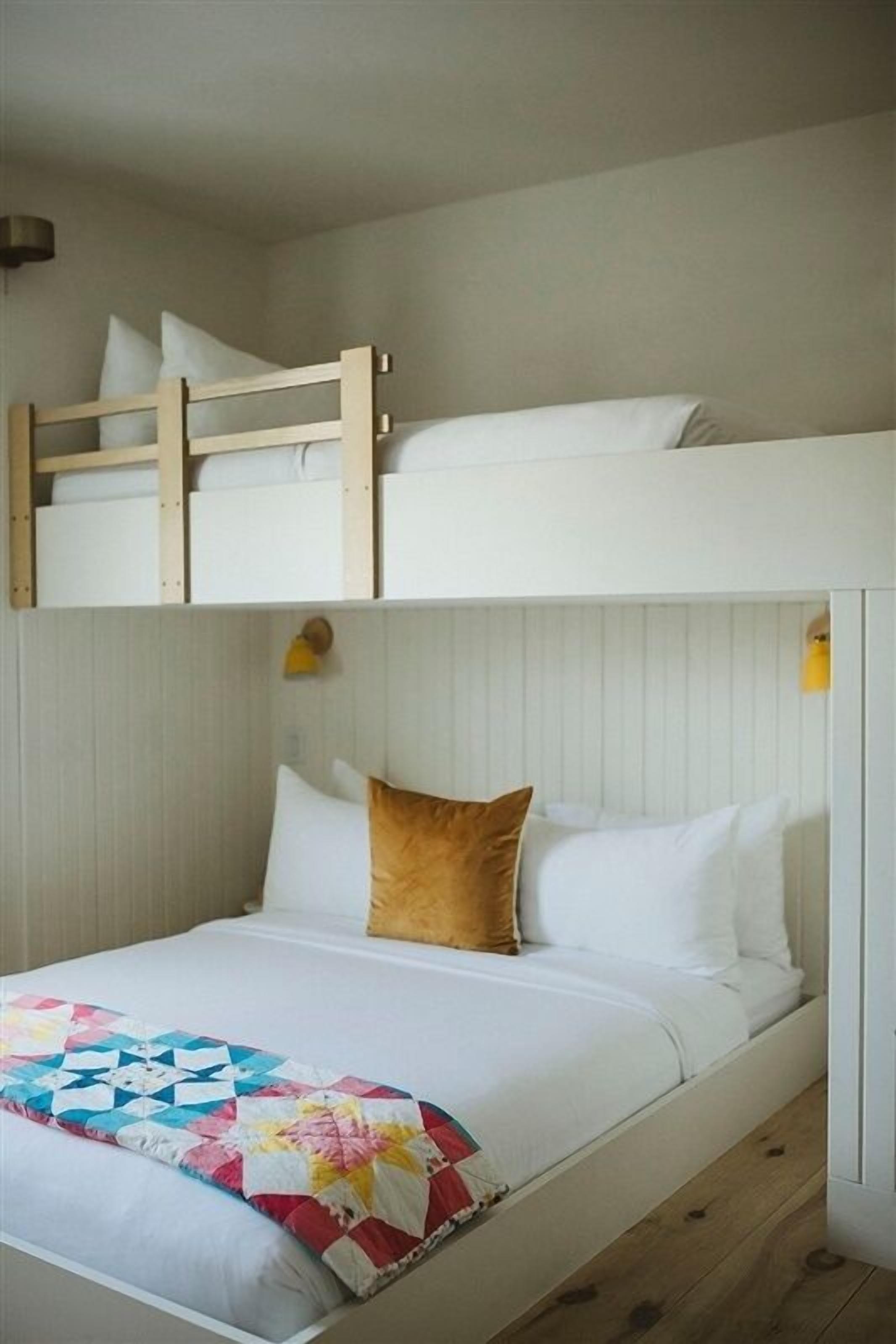 A bunk bed with a wooden ladder, white bedding, and a colorful quilt.