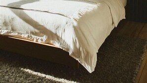 Ein ordentlich bezogenes Bett mit weißen Leinen und gestreiften Kissen, ein gerahmtes Landschaftsbild darüber und ein dunkles Kopfteil.