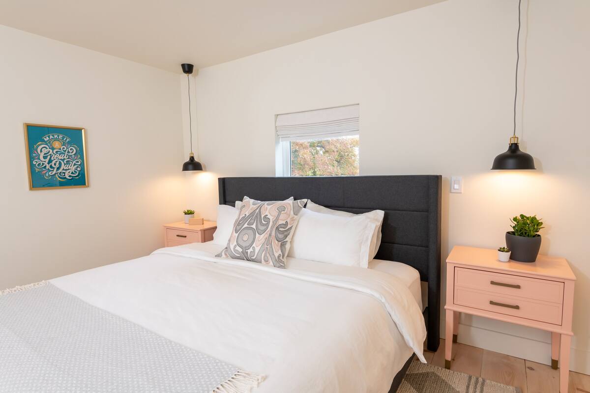 A bedroom with a bed, bedside tables, a window, and a wall-mounted light fixture.