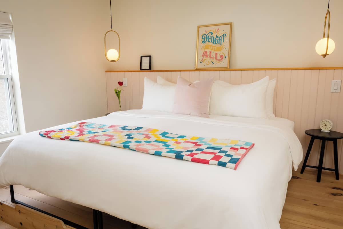 A neatly made bed with a colorful quilt, a small bedside table with a clock, and a framed inspirational quote on the wall.