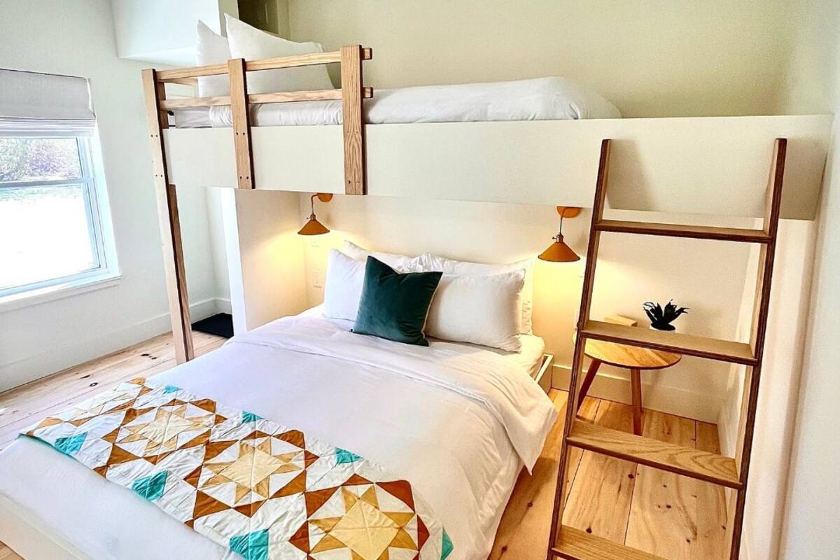 A bunk bed room with a wooden ladder, a bedside table, and a quilt.