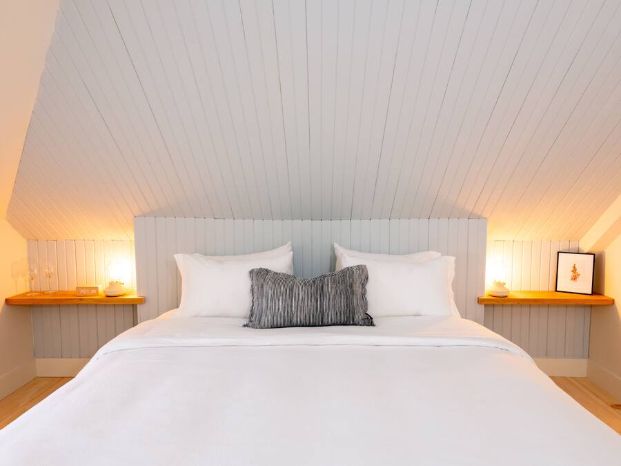 A bedroom with a large bed, two bedside tables with lamps, and a sloped ceiling.