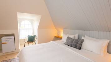 A bedroom with a large bed, a nightstand with a lamp, a chair, and a small white appliance.