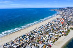 An aerial view of a coastal town with a beach, residential buildings, and a pier.