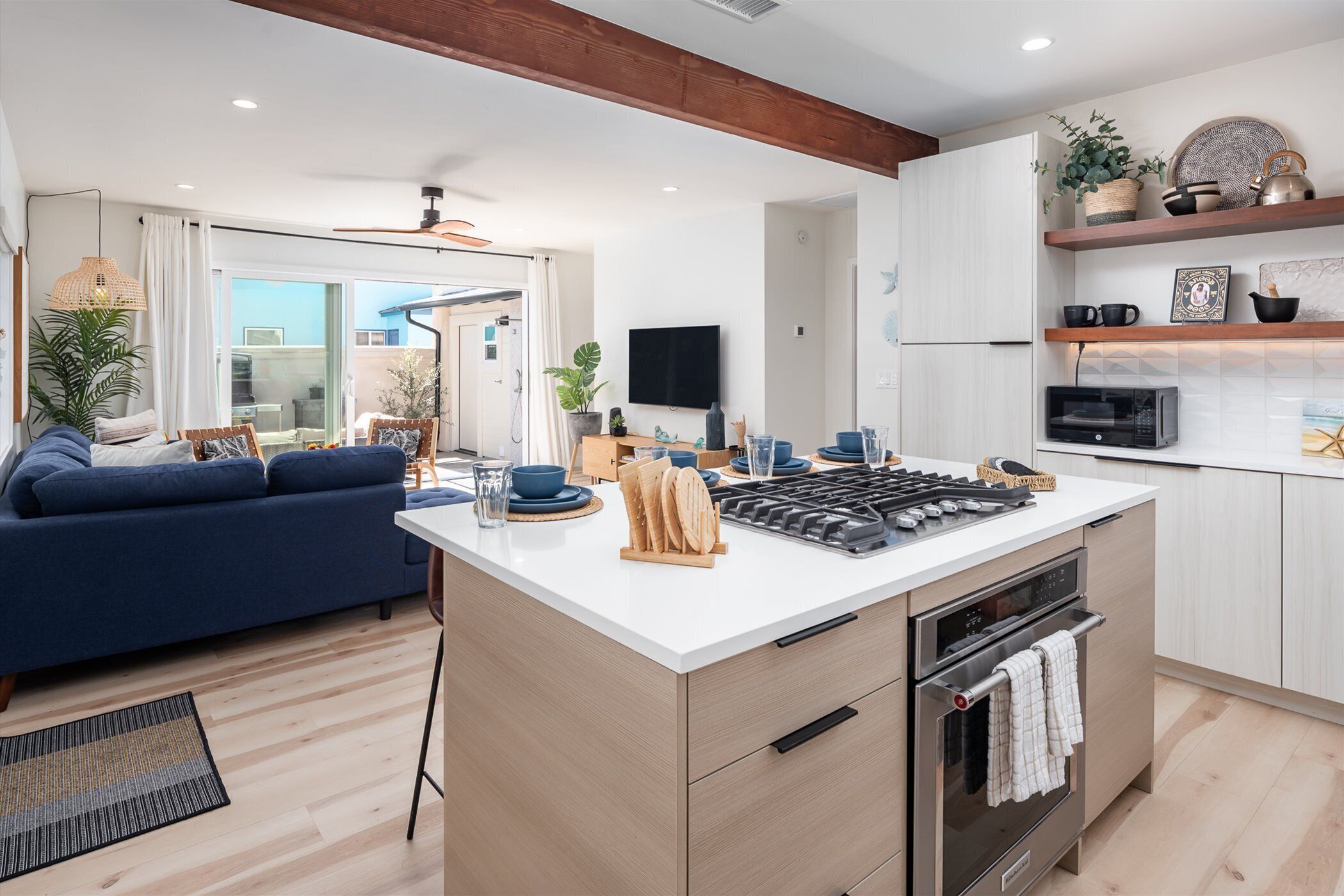 A modern kitchen with an island, built-in oven, and microwave. There is a blue sofa and a dining area with a table and chairs.