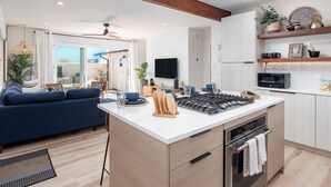 A modern kitchen with an island, built-in oven, and microwave. There is a blue sofa and a dining area with a table and chairs. - Zanzibar Retreat 2BR | Walk to Beach! + Courtyard (San Diego)