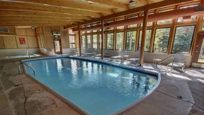 An indoor swimming pool with clear blue water, surrounded by lounge chairs and large windows offering views of the outdoors. - Homestead 2024 (Keystone)