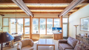 A spacious living room with a wooden ceiling, large windows offering a mountain view, a television, and a cozy seating area. - Homestead 2024 (Keystone)