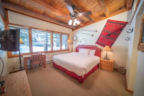 A bedroom with a large bed, wooden ceiling, and a view of the outdoors through large windows.