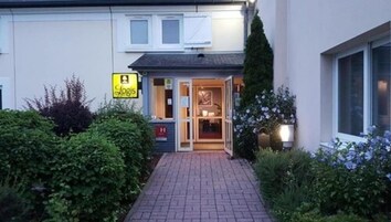 L’entrée d’un hôtel, avec une enseigne indiquant « Logis » et une porte vitrée donnant sur l’intérieur.